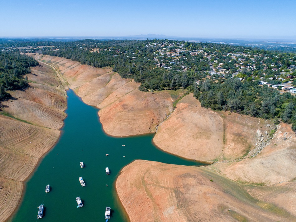 Image of Lake Oroville. The lake is half full with some boats in the middle of the lake. 