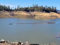 A DWR Civil Maintenance boat uses a long boom line to drag collected driftwood across Lake Oroville (Jan. 28, 2023).